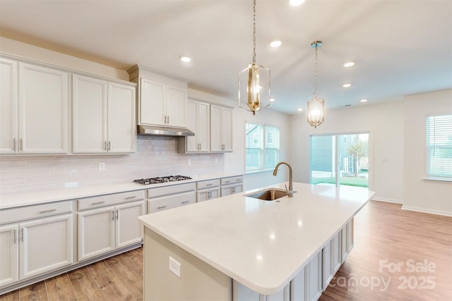 kitchen with stainless steel gas cooktop, under cabinet range hood, a healthy amount of sunlight, and a sink