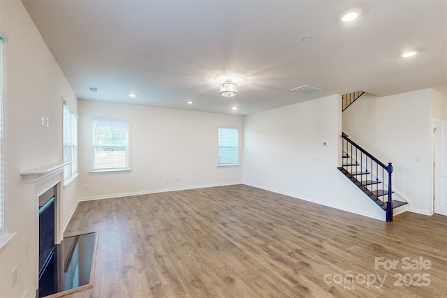 unfurnished living room with a wealth of natural light, stairway, recessed lighting, and wood finished floors