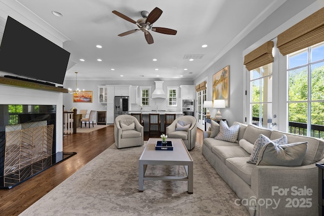 living area featuring ornamental molding, wood finished floors, a ceiling fan, recessed lighting, and a fireplace with raised hearth