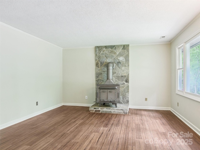 unfurnished living room featuring a wood stove, ornamental molding, a textured ceiling, and wood finished floors
