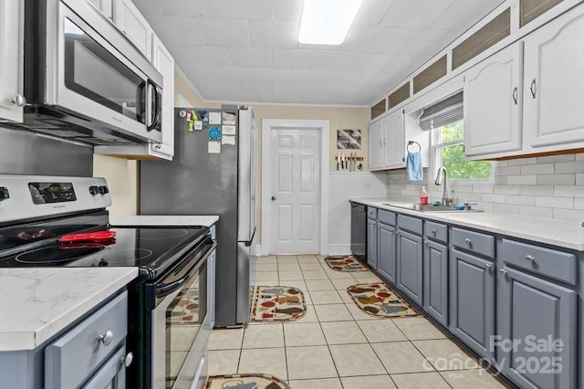 kitchen with a sink, white cabinetry, light countertops, backsplash, and appliances with stainless steel finishes