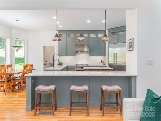 kitchen with a sink, high quality appliances, a breakfast bar area, and under cabinet range hood