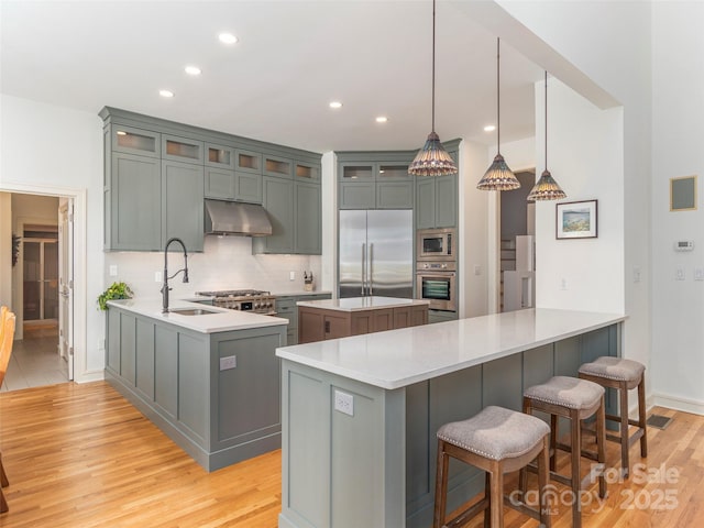 kitchen featuring built in appliances, light wood-style flooring, a peninsula, and under cabinet range hood