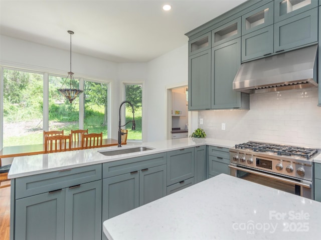 kitchen featuring pendant lighting, under cabinet range hood, a sink, high end stainless steel range, and backsplash
