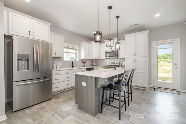 kitchen with a sink, stainless steel appliances, white cabinets, visible vents, and light wood-style floors