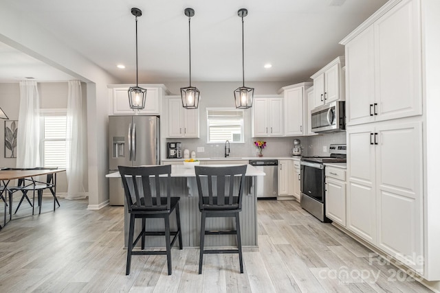 kitchen featuring a center island, a sink, stainless steel appliances, light wood-type flooring, and white cabinetry