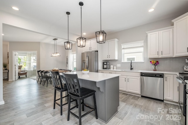 kitchen with a sink, stainless steel appliances, light wood finished floors, backsplash, and a kitchen island