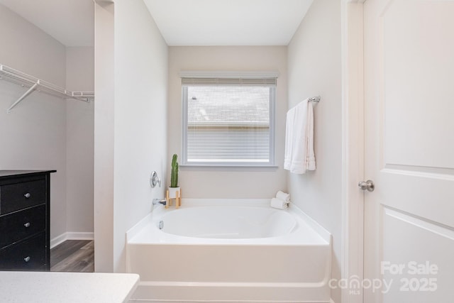bathroom with a walk in closet, a bath, and wood finished floors