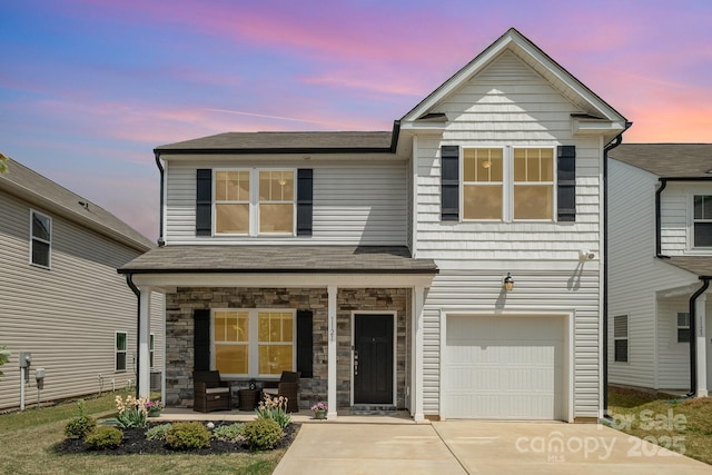 traditional home featuring driveway, covered porch, a garage, a shingled roof, and stone siding