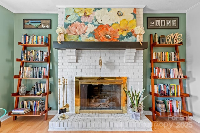 interior space with ornamental molding, a brick fireplace, baseboards, and wood finished floors