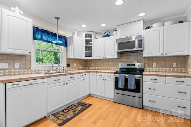 kitchen featuring a sink, appliances with stainless steel finishes, white cabinets, tile countertops, and light wood-style floors