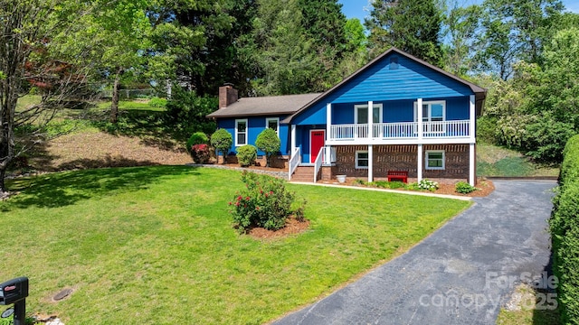 split level home featuring a chimney, driveway, brick siding, covered porch, and a front lawn