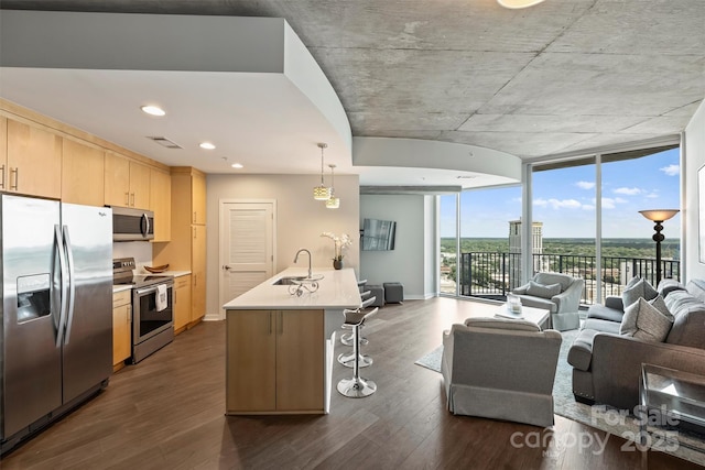 kitchen featuring stainless steel appliances, open floor plan, a breakfast bar area, light brown cabinets, and dark wood-type flooring