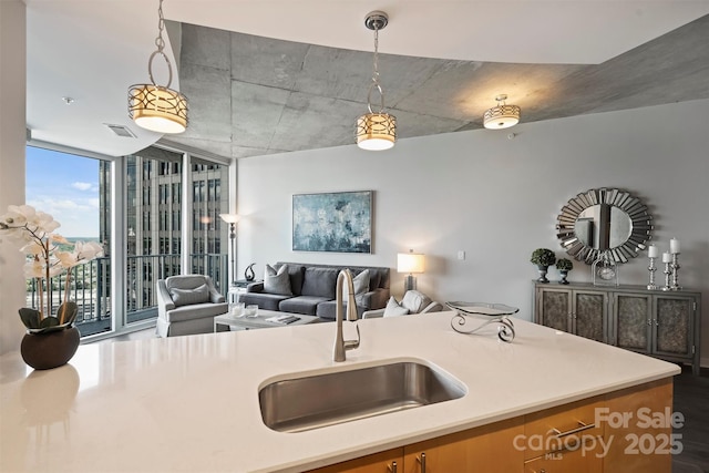 kitchen featuring a sink, open floor plan, light countertops, hanging light fixtures, and a wall of windows
