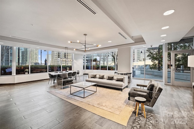 living area with a tray ceiling, a chandelier, wood finished floors, healthy amount of natural light, and recessed lighting