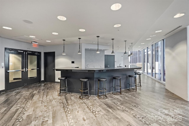 kitchen featuring light wood-style flooring, a large island with sink, dark countertops, french doors, and a breakfast bar area