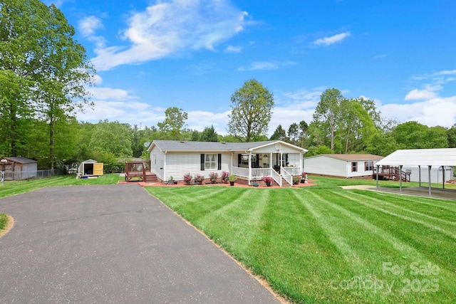 view of front facade with a porch, aphalt driveway, a detached carport, a storage unit, and an outbuilding