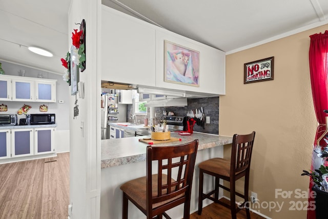 kitchen featuring a breakfast bar area, wood finished floors, freestanding refrigerator, light countertops, and black microwave