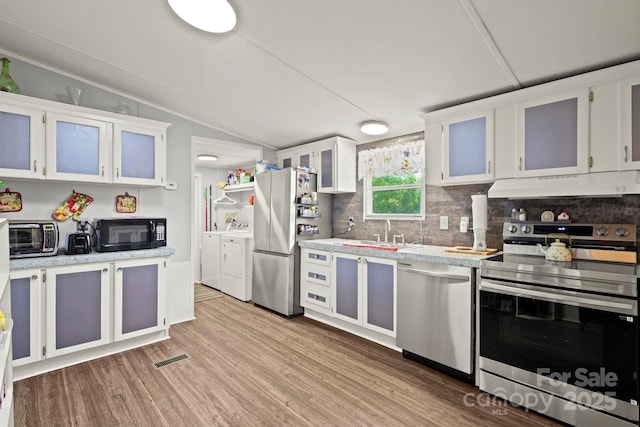 kitchen featuring a sink, washing machine and clothes dryer, stainless steel appliances, under cabinet range hood, and lofted ceiling