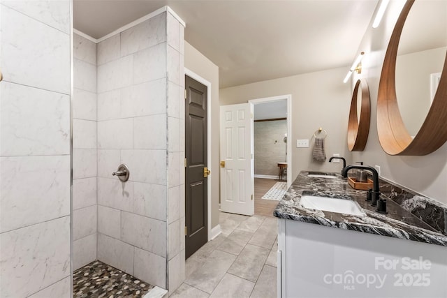 full bath featuring double vanity, tiled shower, tile patterned floors, and baseboards