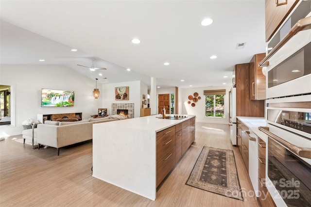 kitchen featuring white appliances, modern cabinets, light wood-style floors, a lit fireplace, and a spacious island