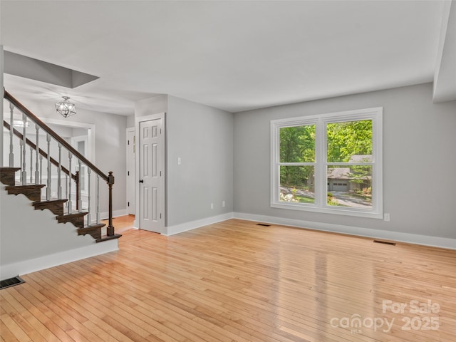 unfurnished living room with a chandelier, hardwood / wood-style flooring, stairs, and baseboards