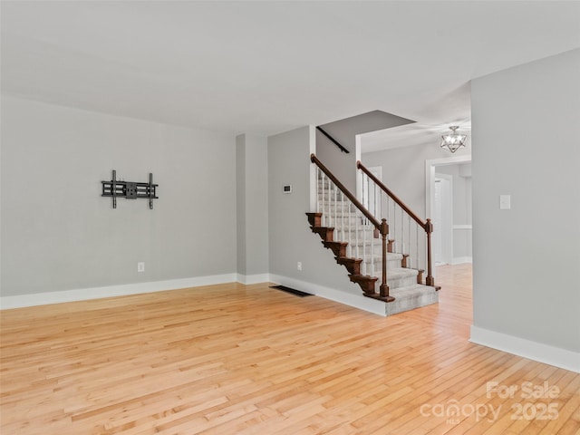 spare room featuring wood finished floors, stairway, a chandelier, and baseboards