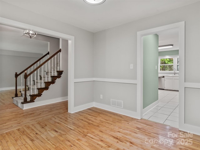 unfurnished room with light wood-style floors, a chandelier, stairway, and baseboards