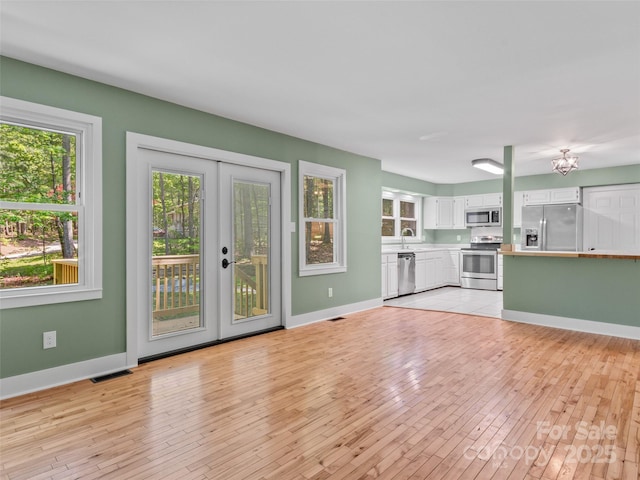 unfurnished living room featuring light wood-style flooring, plenty of natural light, and french doors