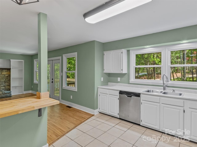 kitchen featuring stainless steel dishwasher, a sink, healthy amount of natural light, and white cabinetry