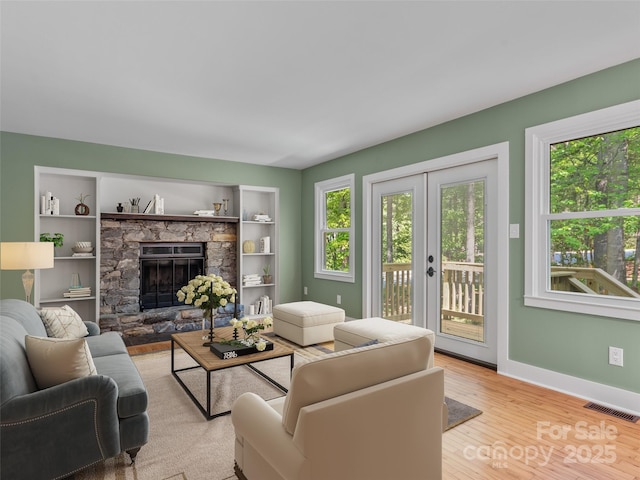 living room featuring a fireplace, light wood-type flooring, baseboards, french doors, and built in features