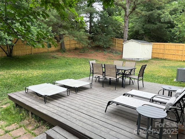 wooden terrace featuring a yard, an outbuilding, outdoor dining space, a fenced backyard, and a storage unit