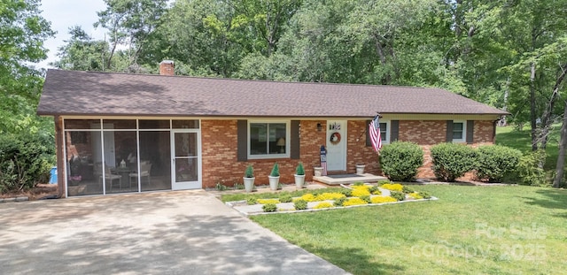 single story home featuring a chimney, brick siding, a sunroom, roof with shingles, and a front lawn