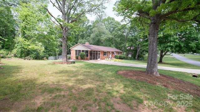 ranch-style house with concrete driveway, a front lawn, a chimney, and brick siding