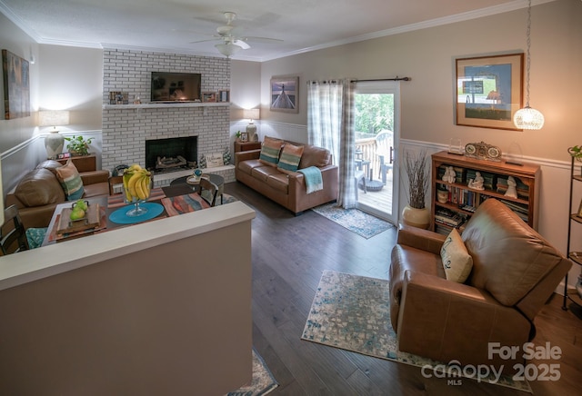 living room with a ceiling fan, ornamental molding, a wainscoted wall, wood finished floors, and a fireplace