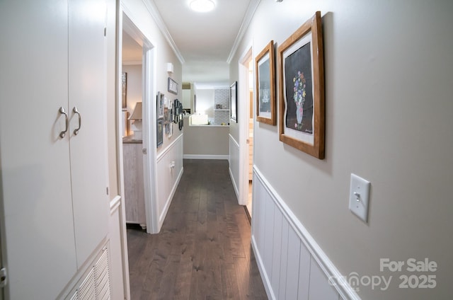 hall featuring dark wood-style flooring, a decorative wall, wainscoting, and crown molding