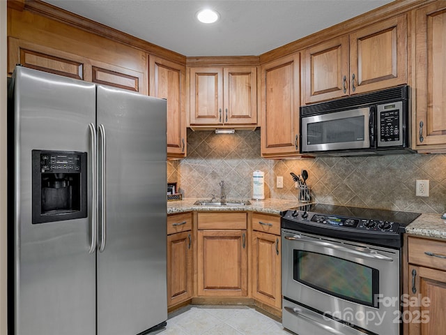 kitchen with appliances with stainless steel finishes, brown cabinetry, light stone counters, and a sink