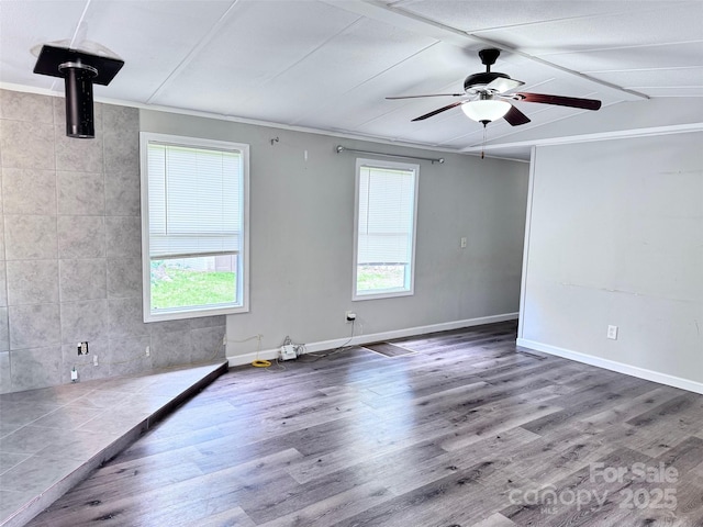 empty room with ceiling fan, wood finished floors, baseboards, and a healthy amount of sunlight
