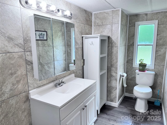 bathroom featuring toilet, tile walls, vanity, and wood finished floors