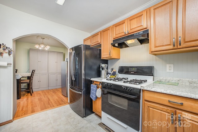 kitchen with under cabinet range hood, freestanding refrigerator, arched walkways, and range with gas stovetop