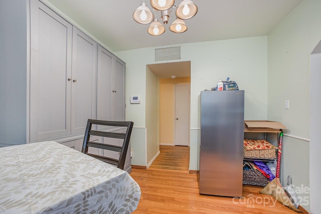interior space with freestanding refrigerator, baseboards, an inviting chandelier, visible vents, and light wood-style floors