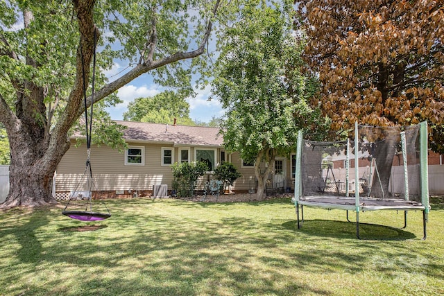 back of property featuring a lawn, a trampoline, central AC unit, and fence