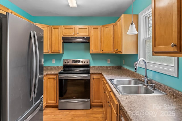 kitchen featuring stainless steel appliances, a sink, under cabinet range hood, light wood-style floors, and pendant lighting
