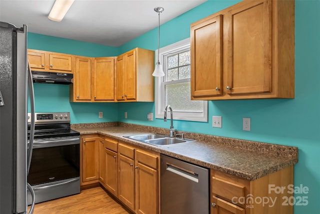 kitchen with appliances with stainless steel finishes, a sink, under cabinet range hood, dark countertops, and pendant lighting