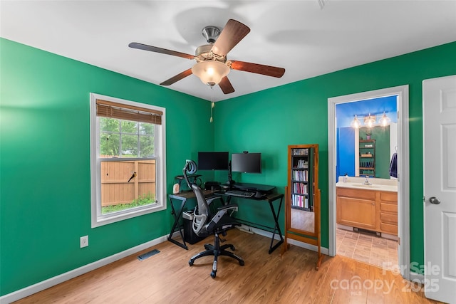 office area with light wood finished floors, a ceiling fan, a sink, and baseboards