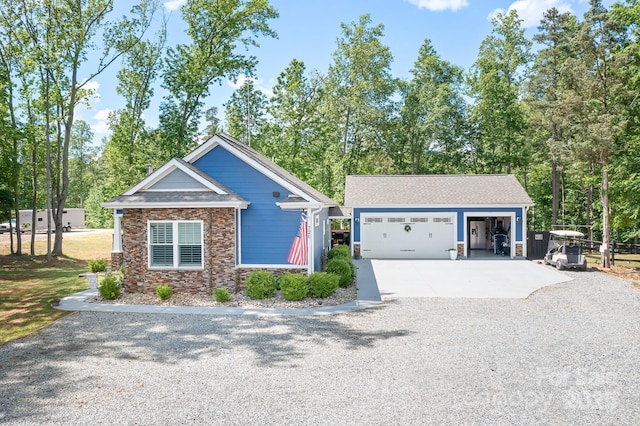 view of front of home with stone siding, an outdoor structure, gravel driveway, view of wooded area, and a garage