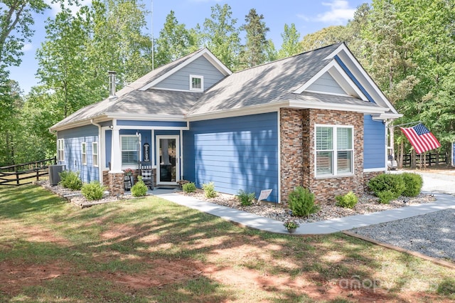 view of front facade with central AC unit, a shingled roof, stone siding, and a porch