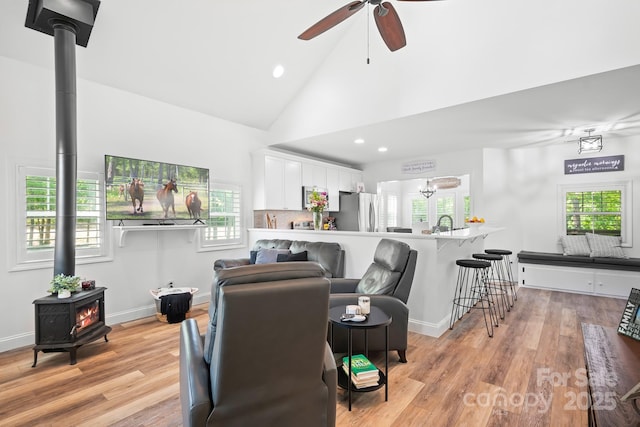 living area featuring a wood stove, ceiling fan, recessed lighting, light wood-style floors, and high vaulted ceiling