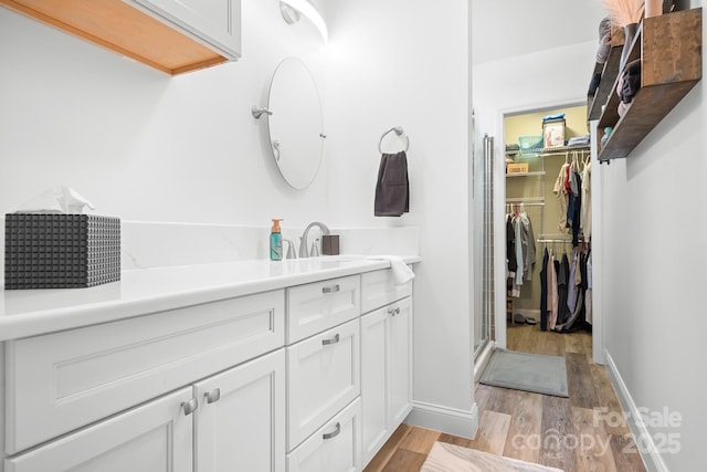 full bathroom with wood finished floors, vanity, a spacious closet, and baseboards