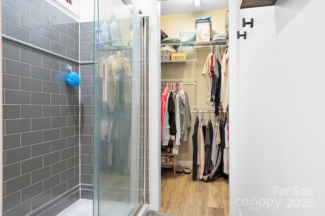 bathroom with a shower stall, wood finished floors, and a walk in closet